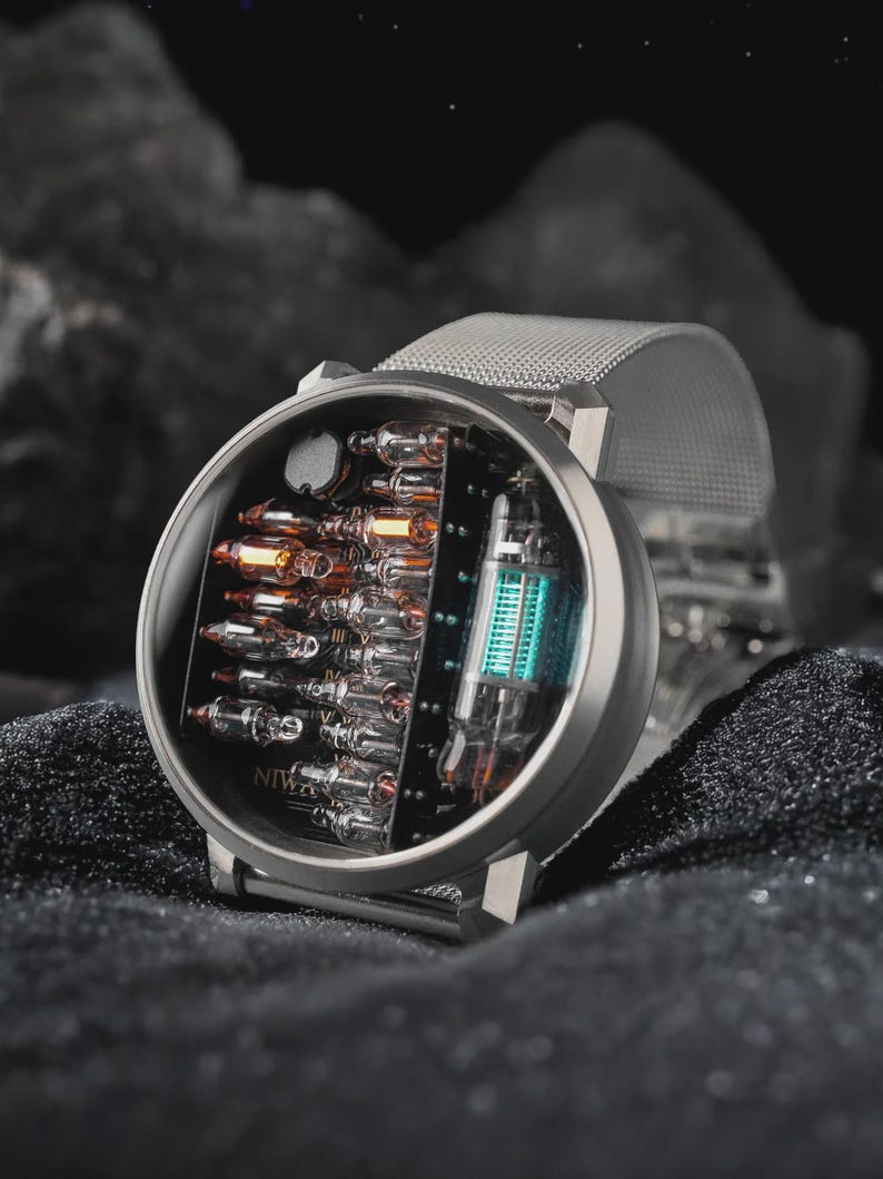 K&ouml;nnte beinhalten: Eine runde Armbanduhr mit silberfarbenem Metall-Mesh-Armband und rundem Geh&auml;use. Das Zifferblatt zeigt eine offene elektronische Anzeige mit mehreren kleinen Glas-Vakuumr&ouml;hren und einer gr&ouml;&szlig;eren leuchtend blauen R&ouml;hre, mit dem Schriftzug NIWA.