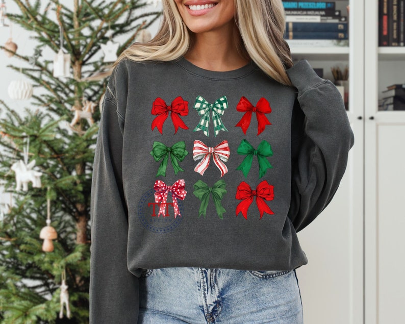 May include: A dark gray sweatshirt with a festive design of nine red and green bows. The bows are arranged in a grid pattern on the front of the sweatshirt.