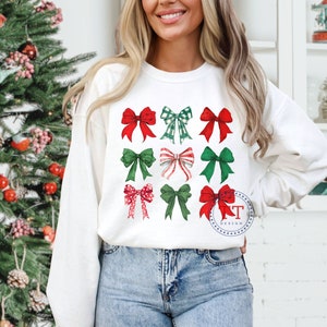 May include: White sweatshirt with a festive design of red and green bows. The bows are arranged in a grid pattern on the front of the sweatshirt.