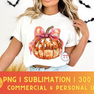K&ouml;nnte beinhalten: Ein wei&szlig;es T-Shirt mit einem Motiv einer Disco-K&uuml;rbis mit einer rosa Schleife. Der K&uuml;rbis ist orange und goldfarben mit einem glitzernden Finish. Der Text "TT Design" befindet sich in der unteren rechten Ecke des Bildes.