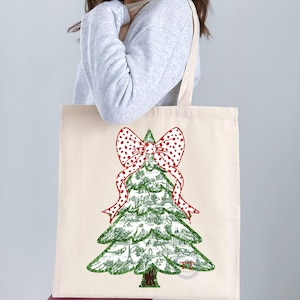 May include: A white canvas tote bag with a green Christmas tree design. The tree is decorated with a red and white polka dot bow.