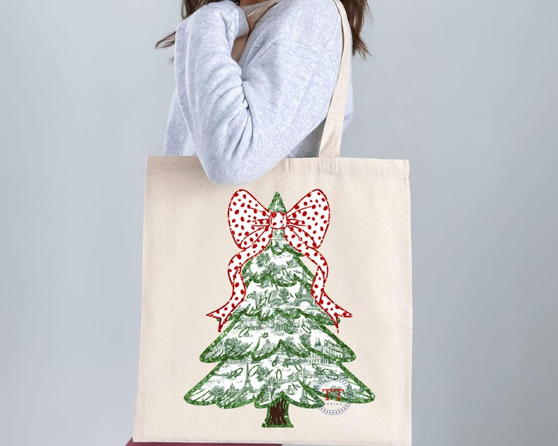 May include: A white canvas tote bag with a green Christmas tree design. The tree is decorated with a red and white polka dot bow.