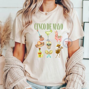 Pu&ograve; includere: Una maglietta bianca con la scritta "Cinco de Mayo" stampata in verde. La maglietta presenta una variet&agrave; di illustrazioni colorate, tra cui una chitarra, una margarita, un lama, uno scheletro, una bottiglia di tequila e un sonagli.