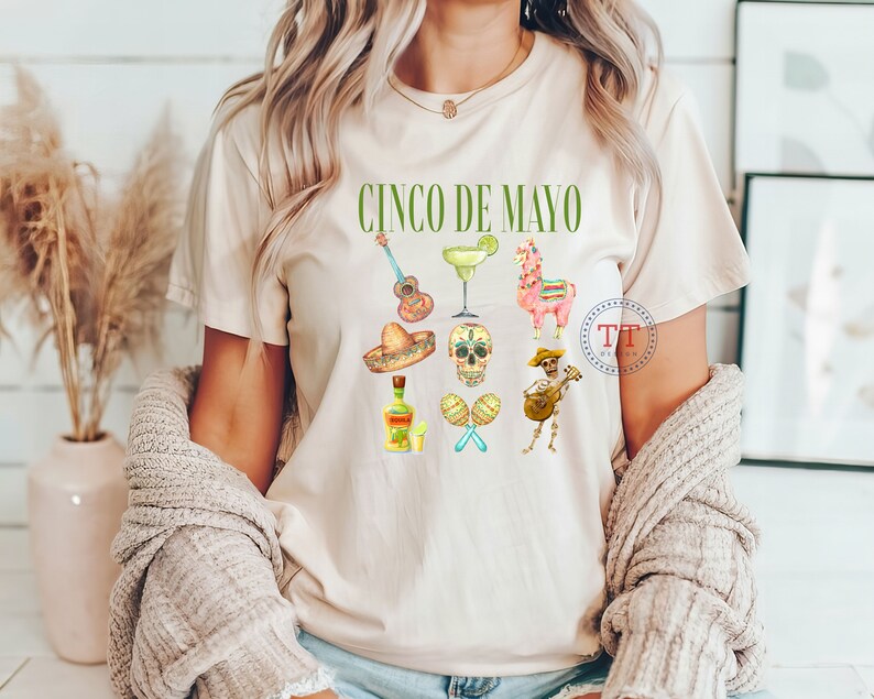 Pu&ograve; includere: Una maglietta bianca con la scritta "Cinco de Mayo" stampata in verde. La maglietta presenta una variet&agrave; di illustrazioni colorate, tra cui una chitarra, una margarita, un lama, uno scheletro, una bottiglia di tequila e un sonagli.