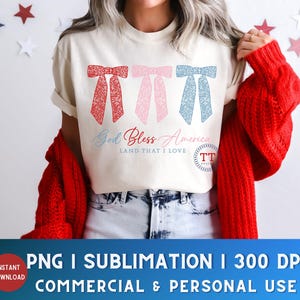 Puede incluir: Una camiseta blanca con tres lazos rojos, rosas y azules con un dise&ntilde;o floral. El texto "God Bless America Land That I Love" est&aacute; impreso en la camiseta.