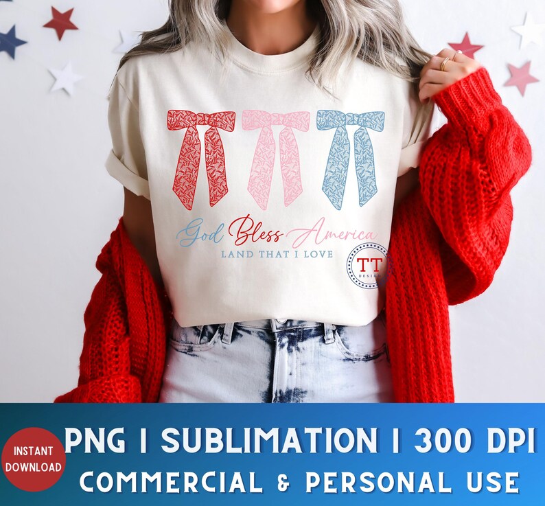 Puede incluir: Una camiseta blanca con tres lazos rojos, rosas y azules con un dise&ntilde;o floral. El texto "God Bless America Land That I Love" est&aacute; impreso en la camiseta.