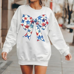 Pu&ograve; includere: Felpa bianca con un grande fiocco rosso, bianco e blu con stelle stampate.