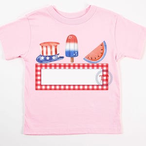 May include: Pink t-shirt with a red, white, and blue watermelon, ice cream, and top hat graphic. The graphic is on a red and white checkered background. The text "The" is printed on the graphic.