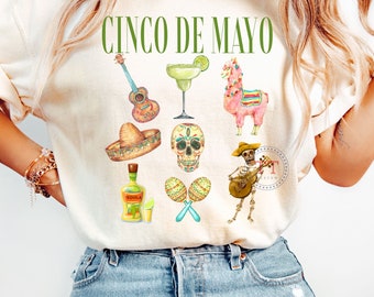 Puede incluir: Una camiseta blanca con el texto "Cinco de Mayo" en letras verdes. La camiseta presenta una variedad de ilustraciones de acuarela de iconos culturales mexicanos, incluyendo una guitarra, una margarita, una llama, un sombrero, una calavera, maracas y un esqueleto tocando una guitarra.