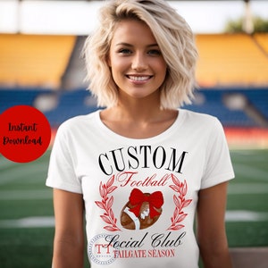 May include: White t-shirt with black text that reads "CUSTOM Football Social Club TAILGATE SEASON". A red bow is on top of a brown football with green leaves around it.