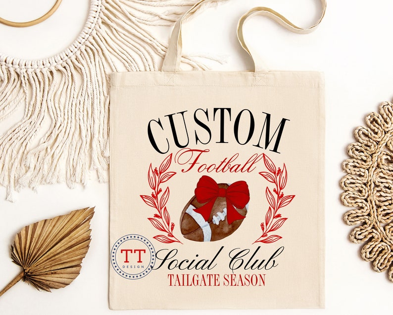 May include: A white canvas tote bag with black text that reads "CUSTOM Football Social Club TAILGATE SEASON". A red bow is on top of a brown football with red and green leaves around it. The text "TT DESIGN" is in a circle in the lower left corner.
