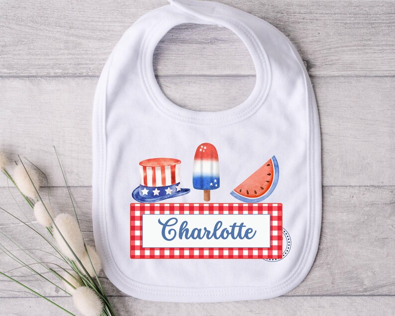 May include: White bib with a red, white, and blue checkered border. The bib features a red, white, and blue hat, a red, white, and blue popsicle, and a red watermelon slice. The text "Charlotte" is printed in blue on the bib.