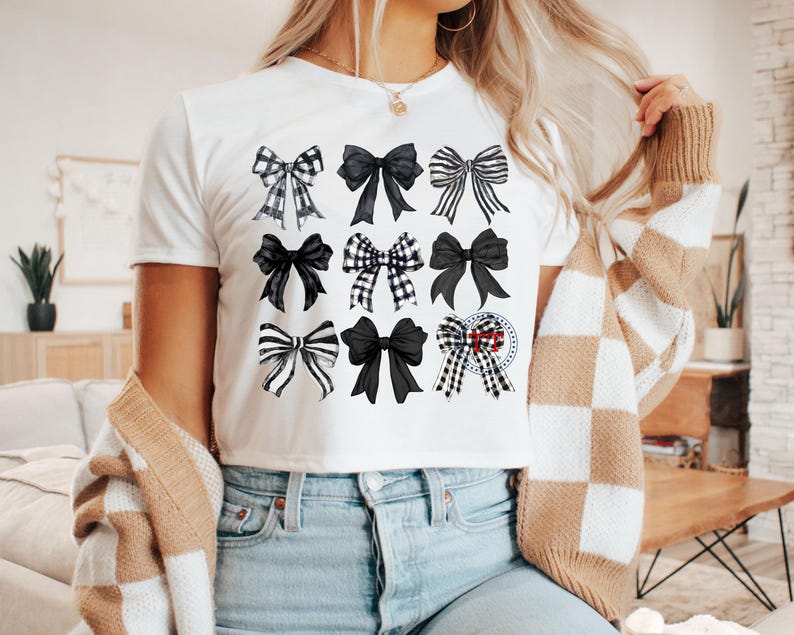 May include: White t-shirt with a black and white bow pattern. The bows are arranged in a grid pattern on the front of the shirt.
