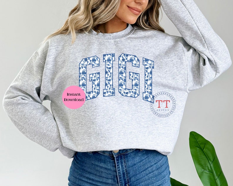 May include: A grey sweatshirt with the word "GIGI" printed in a blue and white floral pattern. The word is in a large, bold font. The sweatshirt is being worn by a person.
