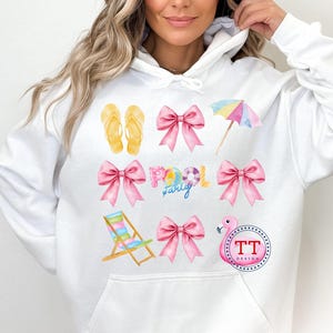 May include: White hoodie with a pink flamingo, beach chair, flip flops, bow, and umbrella design. The text "Family Pool Party" is printed on the hoodie.