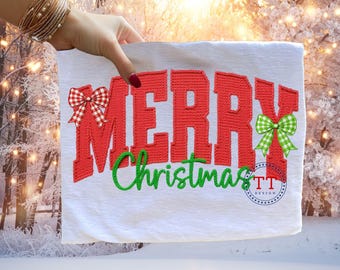 Può includere: Tessuto bianco con le parole "MERRY Christmas" ricamate in rosso e verde. La parola "MERRY" ha un fiocco a scacchi rosso e bianco a sinistra e un fiocco a scacchi verde e bianco a destra. Il design include un logo "TT DESIGN".