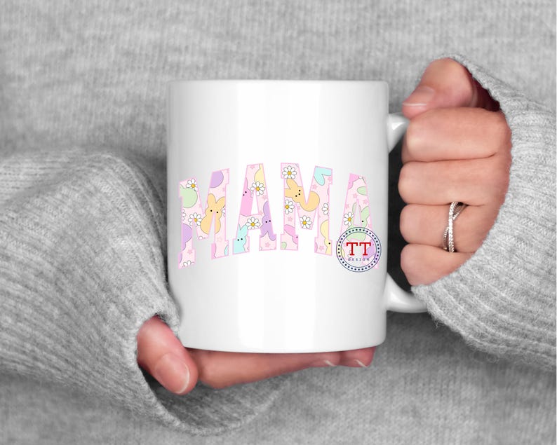 Puede incluir: Taza de cer&aacute;mica blanca con un dise&ntilde;o rosa y blanco con la palabra "MAMA" en una gama de colores pastel. El dise&ntilde;o incluye peque&ntilde;os conejos y flores de colores pastel.