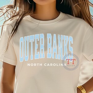 May include: White t-shirt with a blue graphic that says "Outer Banks North Carolina".
