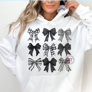 May include: White hoodie with a black and white bow design. The bows are arranged in a grid pattern and are all different sizes and shapes.