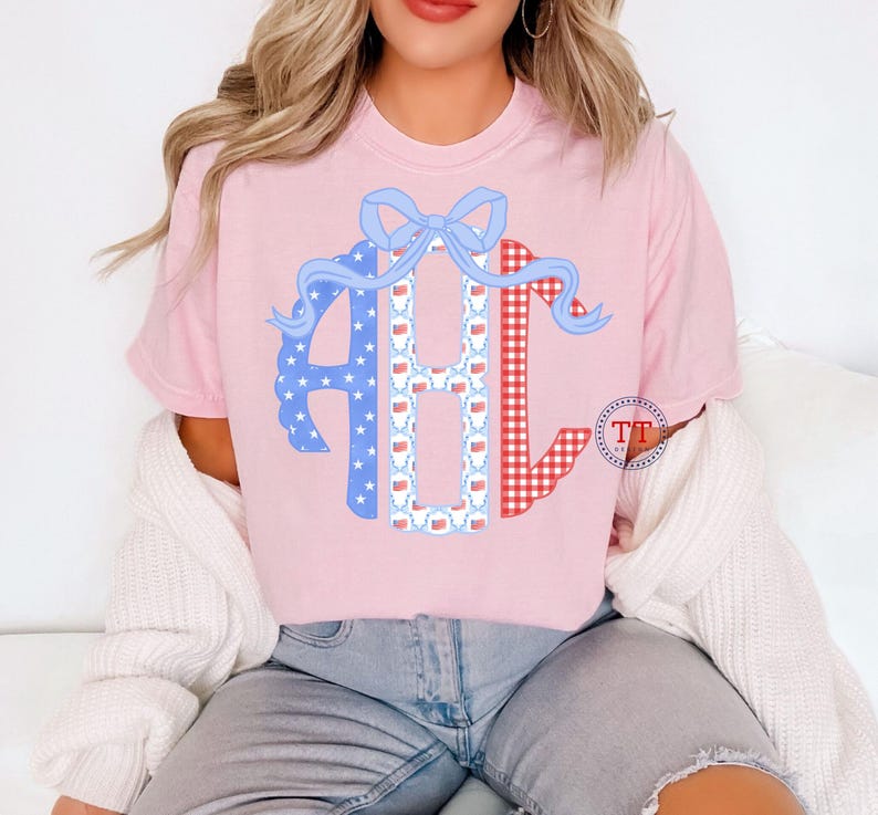 May include: Pink t-shirt featuring a monogram design with the letters ABC. The letter A is blue with white stars, B is white with red and blue patterns, and C is red gingham. A blue bow tops the design.