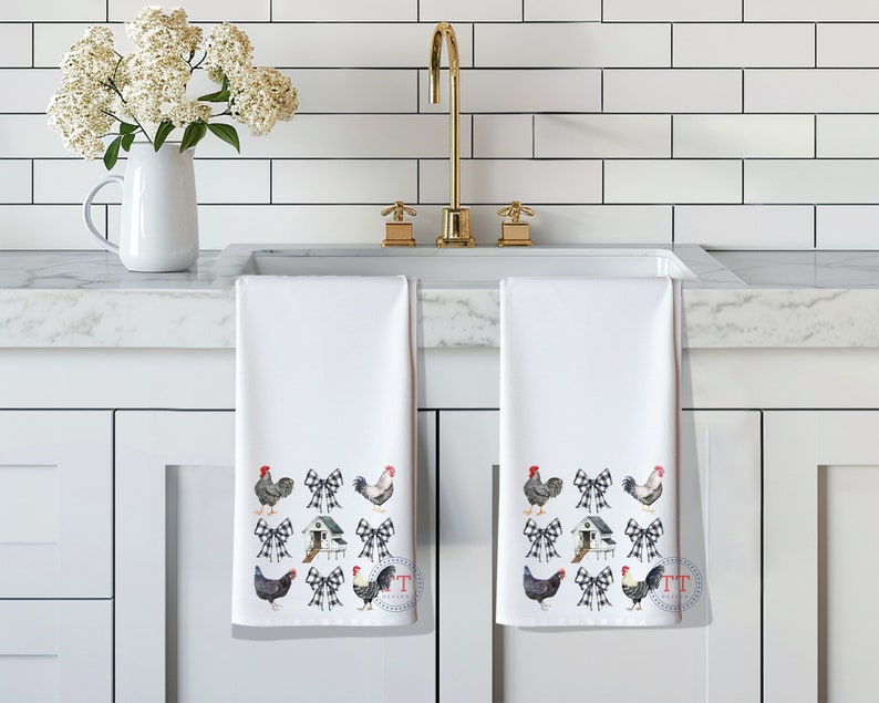 May include: Two white kitchen towels with a black and white checkered bow and chicken design. The towels are hanging on a white kitchen counter.