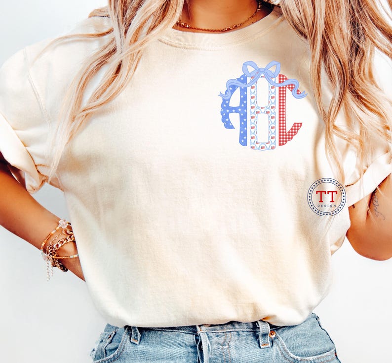 May include: Cream-colored t-shirt featuring a monogram design with the letters "ABC". The letters are decorated with blue polka dots, red gingham, and a blue bow. The shirt has short sleeves and a relaxed fit. The logo "TT DESIGN" is on the lower right.