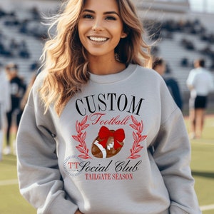 May include: Gray sweatshirt with the text "CUSTOM Football Social Club TAILGATE SEASON" and a football with a red bow on top.
