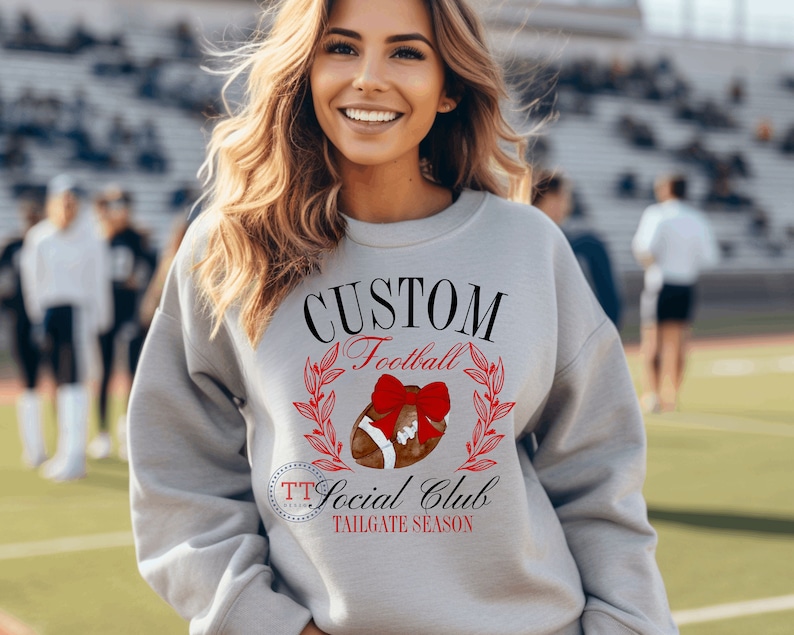 May include: Gray sweatshirt with the text "CUSTOM Football Social Club TAILGATE SEASON" and a football with a red bow on top.