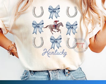 Könnte beinhalten: Ein Sublimationsdesign mit einem Pferd und einem Jockey, umgeben von blauen Schleifen und silbernen Hufeisen. Der Text "Kentucky" steht unter dem Pferd und dem Jockey.