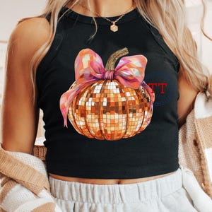 K&ouml;nnte beinhalten: Ein schwarzes Tanktop mit einem goldenen Glitzerk&uuml;rbis mit einer rosa Schleife. Der K&uuml;rbis hat ein Discokugel-Design.