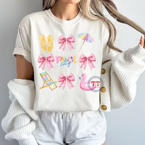 May include: A white t-shirt with a pink and yellow summer themed design. The design includes flip flops, bows, a beach chair, a flamingo float, and the words "Pool Party".