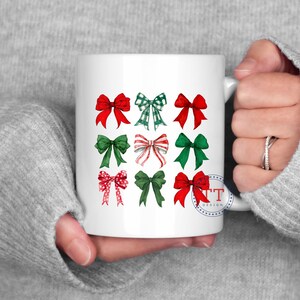 May include: White ceramic mug with a design of nine red and green bows. The bows are arranged in three rows of three. The mug has a blue and white stamp with the text "TT Design".