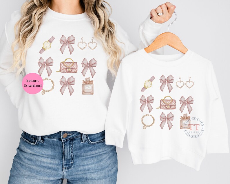 May include: Two white t-shirts with a pink bow and gold accessories design. The design includes a watch, earrings, a purse, a bracelet, and perfume bottle.