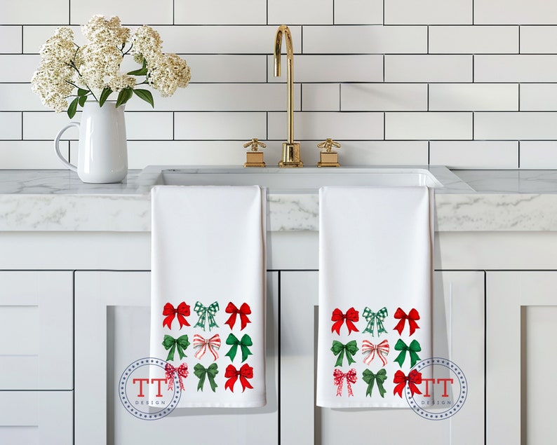 May include: Two white kitchen towels with red and green bows printed on them. The towels are hanging on a white kitchen cabinet.