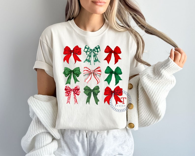 May include: White t-shirt with a design of nine red and green bows. The bows are arranged in three rows of three. The shirt has a crew neck and short sleeves.