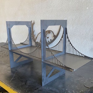 Könnte beinhalten: Ein Regal aus Metall in Form der Golden Gate Bridge mit einem Panda-Silhouetten-Design. Das Regal ist aus schwarzem Metall und hat drei Regalböden.
