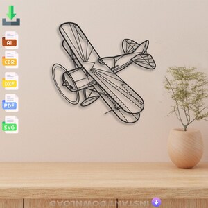 May include: Black metal biplane wall art. The biplane features detailed line work, including the wings, propeller, and tail. The artwork is mounted on a light beige wall above a wooden surface. A small plant in a beige pot is to the right.