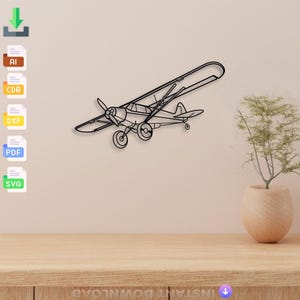 Puede incluir: Arte de pared de avión de metal negro. El avión presenta una hélice, alas y cola, con un contorno detallado. La obra de arte está montada en una pared de color claro sobre una superficie de madera.