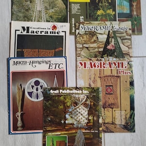 May include: A collection of vintage macrame books with titles like "Macrame Elegance," "Creations in Macrame," and "How to Make Plant Hangers." The covers feature images of macrame projects, including plant hangers and wall hangings. The books are in various sizes and colors.