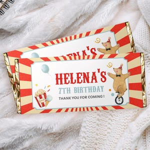 May include: Two red, white, and blue circus-themed chocolate bar wrappers with a bear on a unicycle. The text on the wrapper reads "Helena's 7th Birthday. Thank you for coming!"