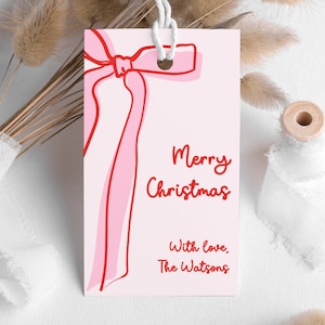 May include: A pale pink gift tag featuring a red bow design and the words "Merry Christmas" in red script. The tag also includes "With love, The Watsons". It is tied with a white string.