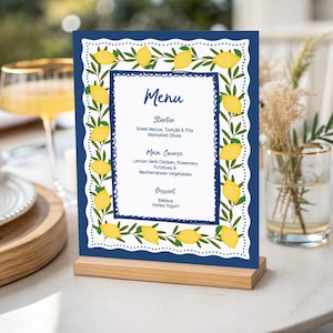 May include: A rectangular menu card standing on a light wood base, featuring a dark blue border with a white scalloped edge and a pattern of yellow lemons and green leaves. The center white panel displays the text Menu, Starter, Main Course, and Dessert.