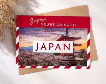 May include: A red and white striped card with the text "Surprise You're Going To... Japan" in white. The card features a photo of a Japanese pagoda with cherry blossoms in the foreground.
