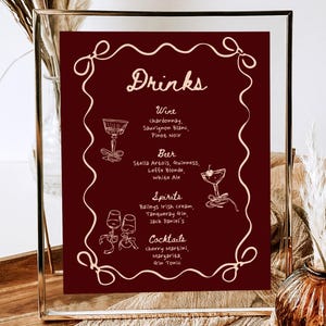 May include: A framed drinks menu with a burgundy background and white text. The menu lists wine, beer, spirits, and cocktails. The text is handwritten and includes a variety of drinks.
