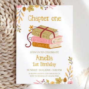 May include: A white rectangular birthday invitation card featuring a stack of three illustrated books tied with a red ribbon. The text reads Chapter one, JOIN US TO CELEBRATE Amelia 1st Birthday, SUNDAY 10.11.20XX 3:00 PM, 21 BOOKS AVENUE, LOS ANGELES CA, RSVP TO HELENA AT 123.456.7890. The design is decorated with colourful autumn leaves.