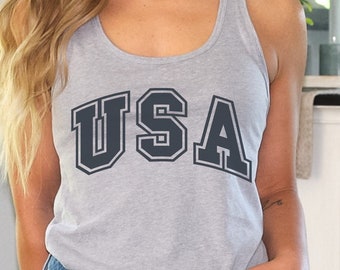 May include: A gray tank top with the word "USA" printed in black letters. The tank top is being worn by a person with long blonde hair. The person is wearing denim shorts.