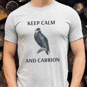 Puede incluir: Una camiseta gris con el texto "Keep Calm and Carrion" y una ilustraci&oacute;n en blanco y negro de un buitre.