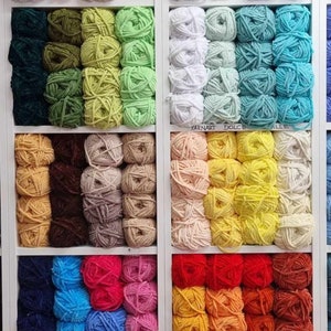 May include: A shop display of colourful yarn balls in a white shelving unit. The yarn is arranged by colour, including pink, green, blue, yellow, and red. The yarn is likely for knitting or crochet projects.