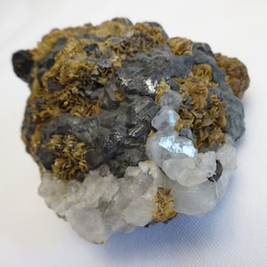 Könnte beinhalten: Ein Cluster aus grauen, schwarzen und braunen Mineralien mit einigen klaren, glasartigen Kristallen. Die Mineralien sind in einer groben, natürlichen Form angeordnet.