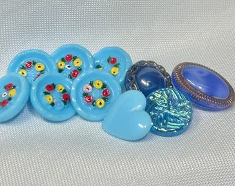 May include: Assortment of blue glass buttons with floral and heart designs. Some buttons have a shiny iridescent finish.